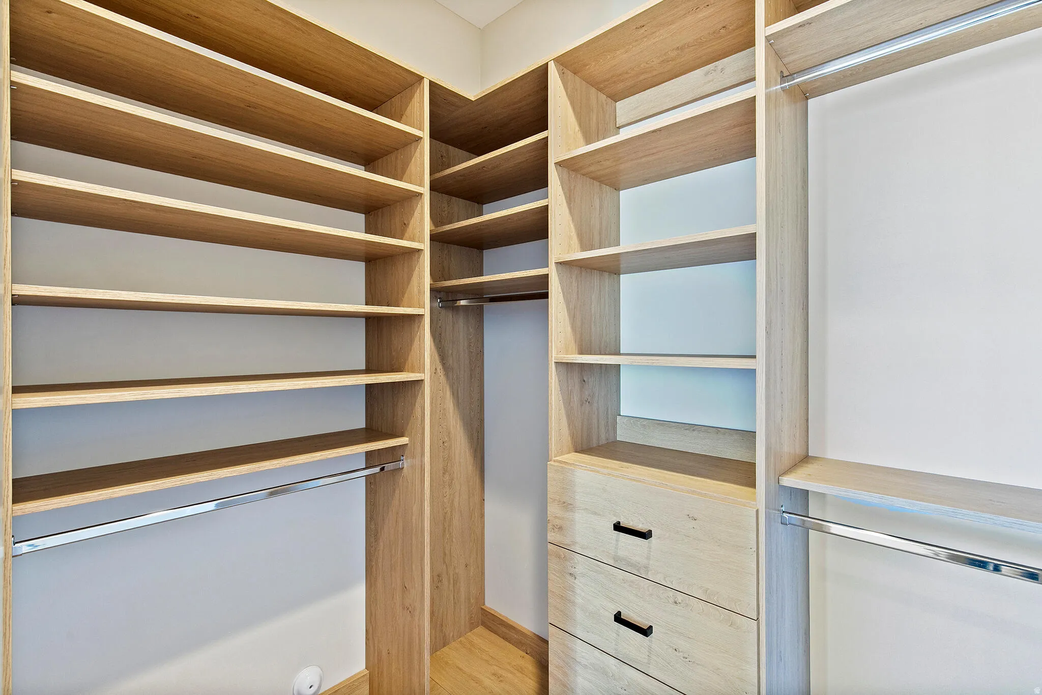 Custom closet system featuring wood-finish shelving, built-in drawers with dark hardware, and chrome hanging rods