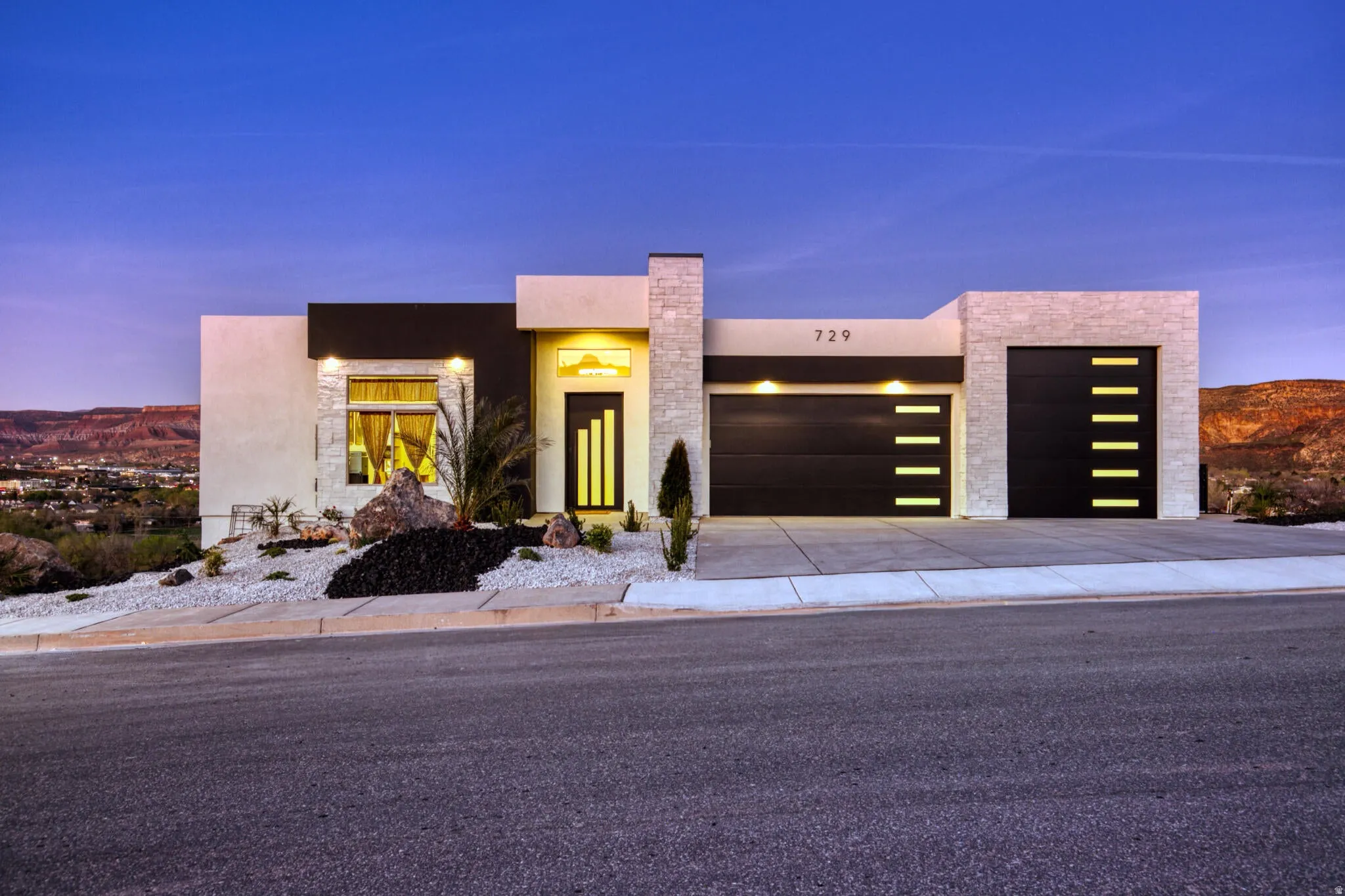 Modern architectural home featuring a multi-tone exterior, two integrated garage doors with horizontal light accents, and xeriscaped landscaping