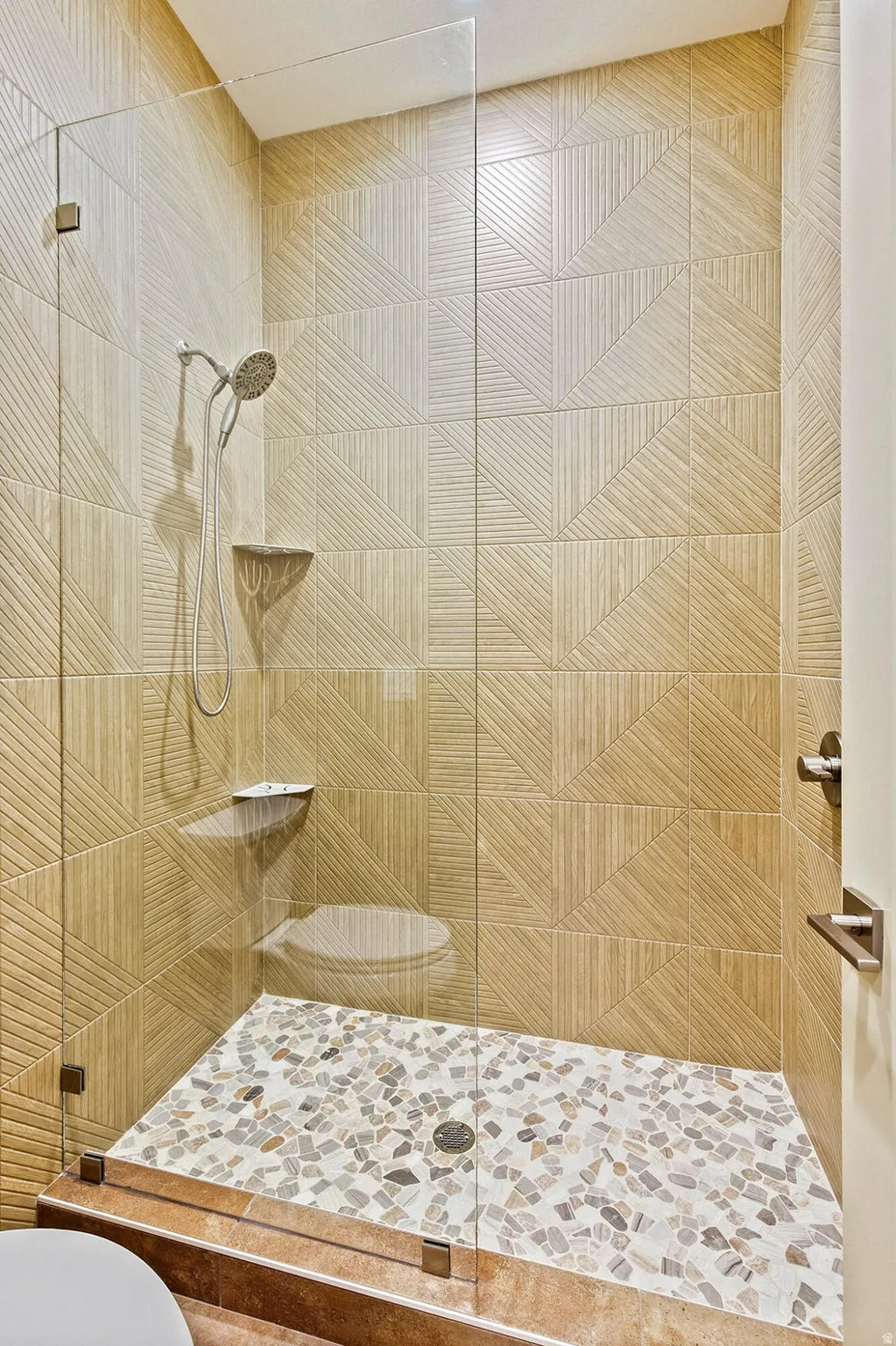 Walk-in shower featuring a frameless glass enclosure, pebble-tile flooring, and textured wall tiling