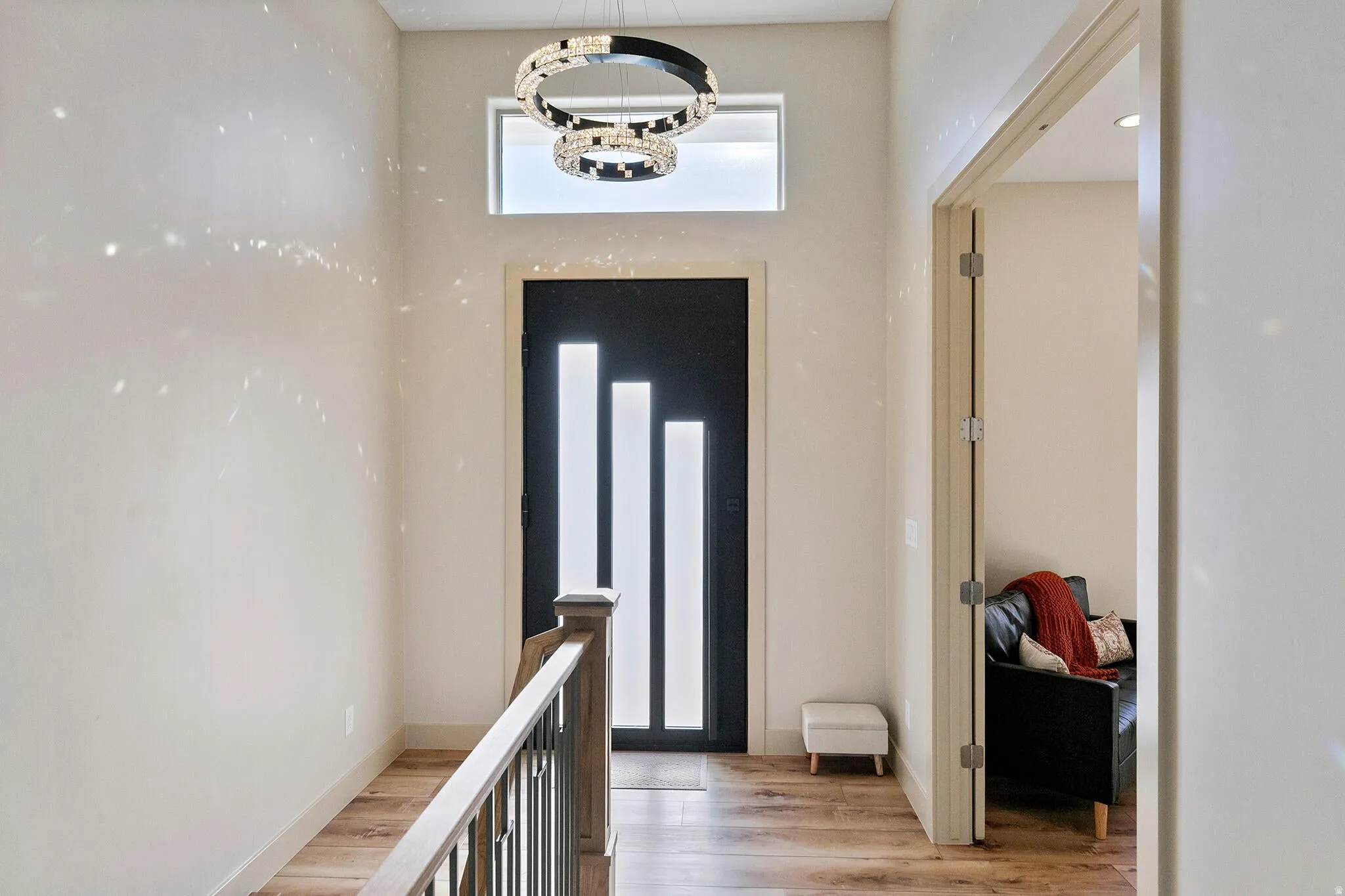 Entryway featuring a modern black door with vertical glass inserts, transom window, contemporary chandelier, wood-finish flooring, and a staircase with a wooden handrail and metal balusters