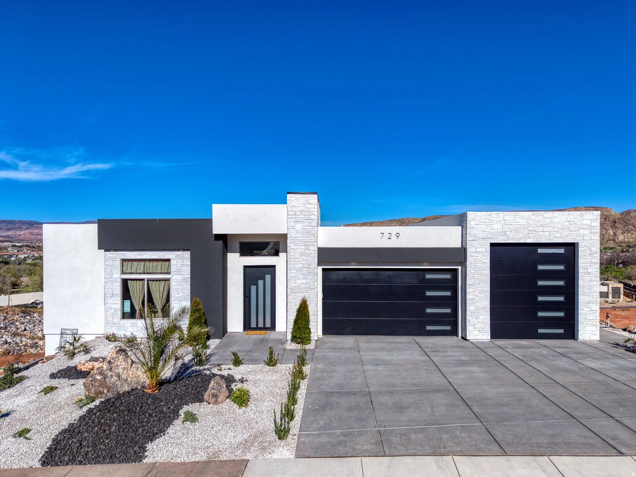 Modern exterior featuring a prominent black and white facade, stacked stone accents, a dark entry door with vertical glass inserts, and two black garage doors with horizontal window panels