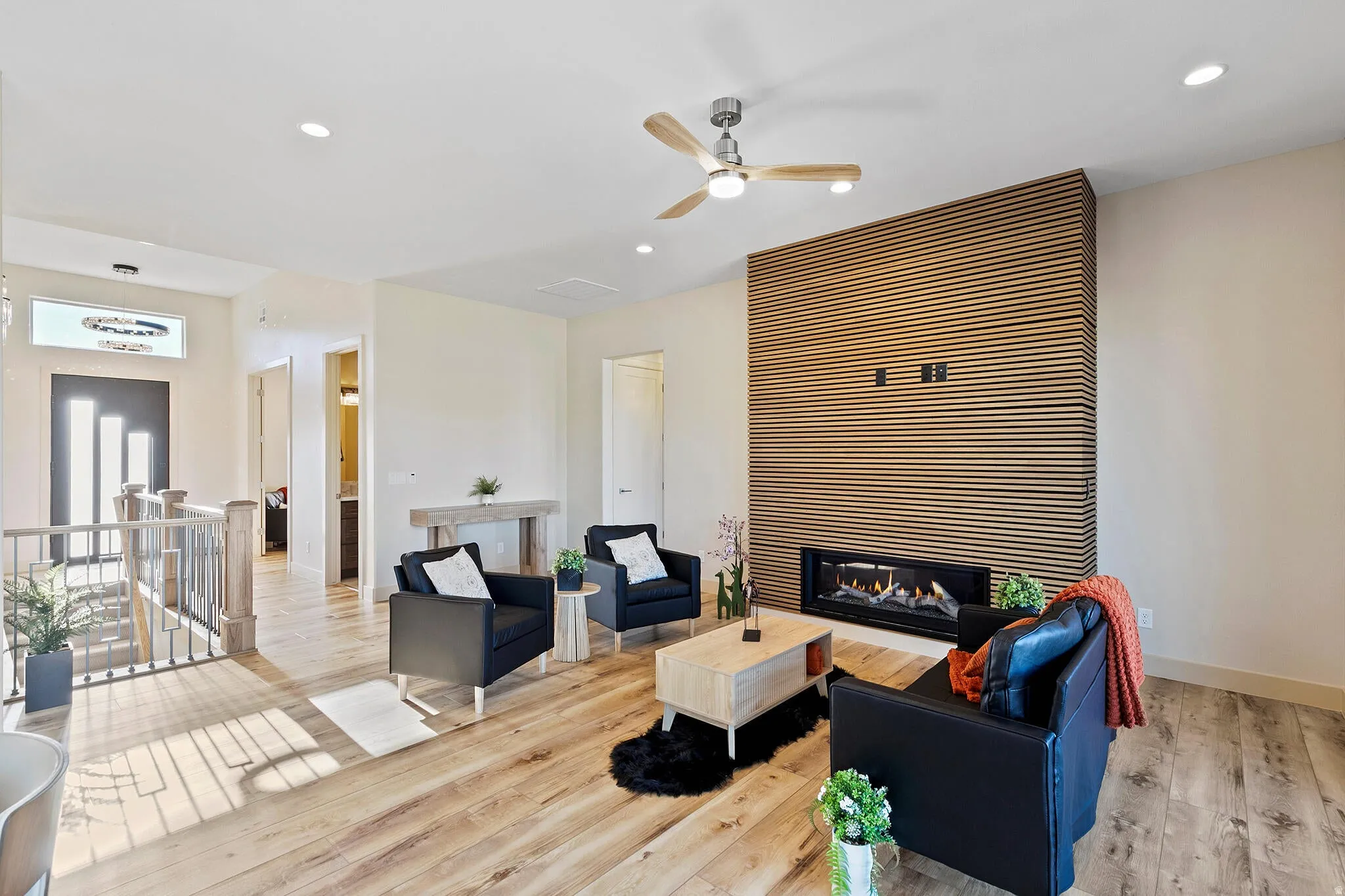 Spacious living area featuring a contemporary linear fireplace with a slatted wood accent wall, wood-finish flooring, recessed lighting, and a ceiling fan