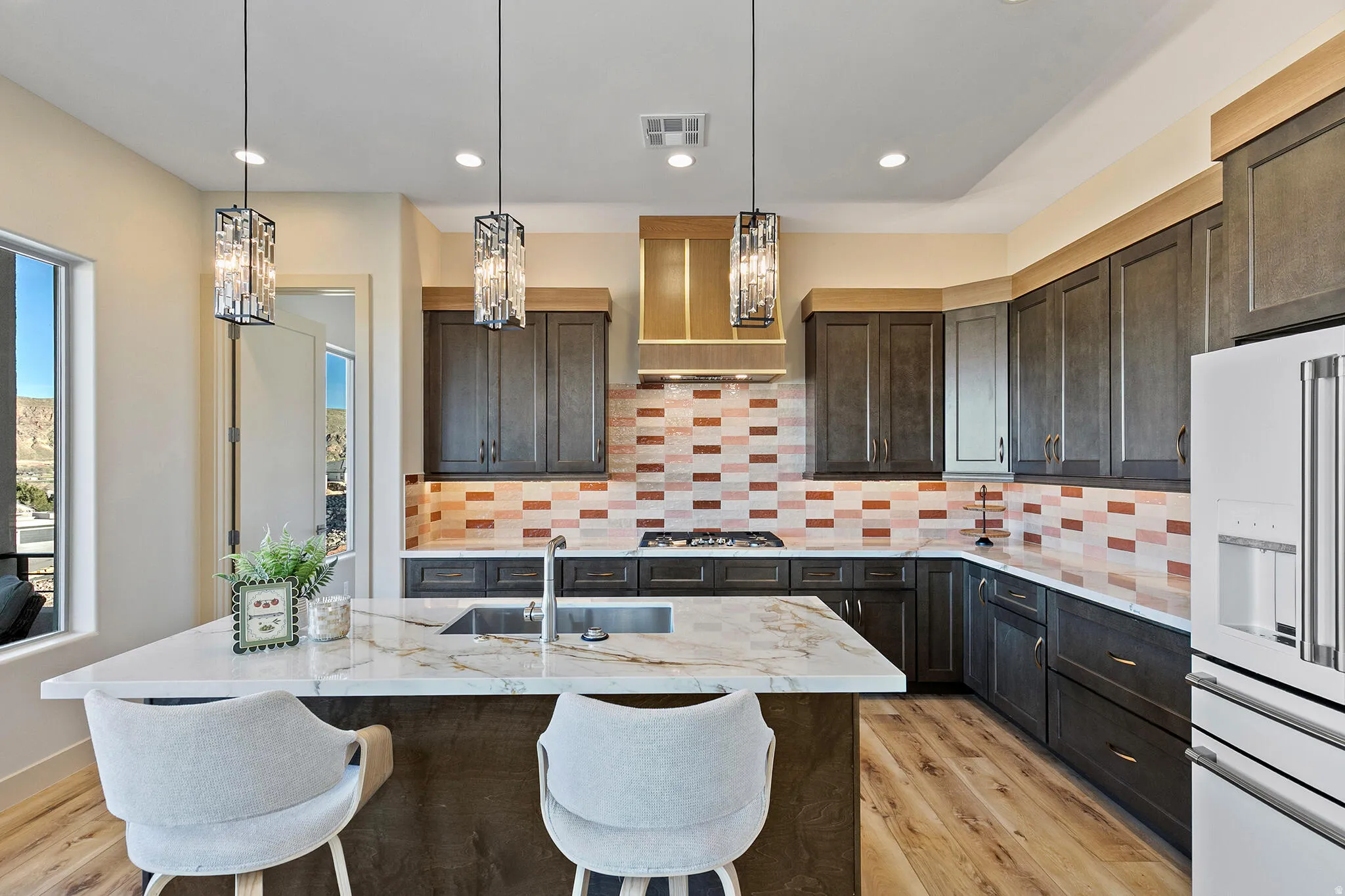 Kitchen featuring a central island with a waterfall countertop, dark wood-finish cabinetry, a gas range with an overhead vent hood, a tiled backsplash, and recessed lighting