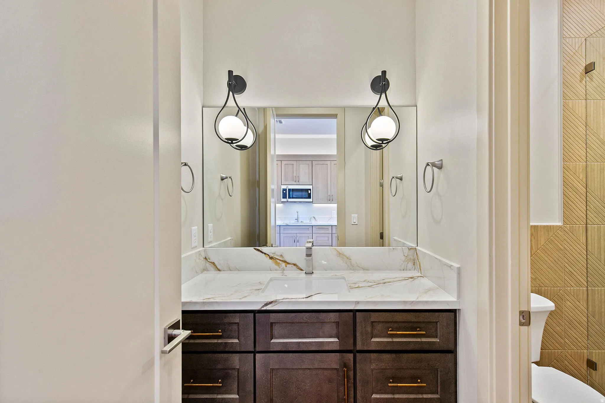 Bathroom vanity with a white countertop featuring gold-toned veining, dark wood-finish cabinetry, and gold-tone hardware