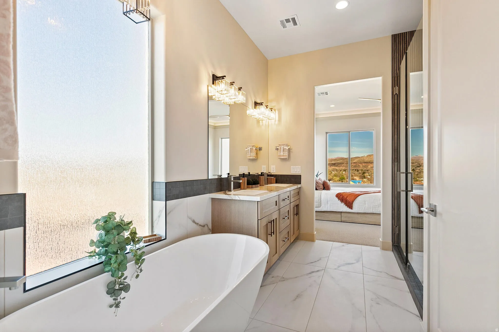 Freestanding bathtub with an expansive frosted window, dual vanity with undermount sinks, decorative light fixtures, and marble-finish tile flooring