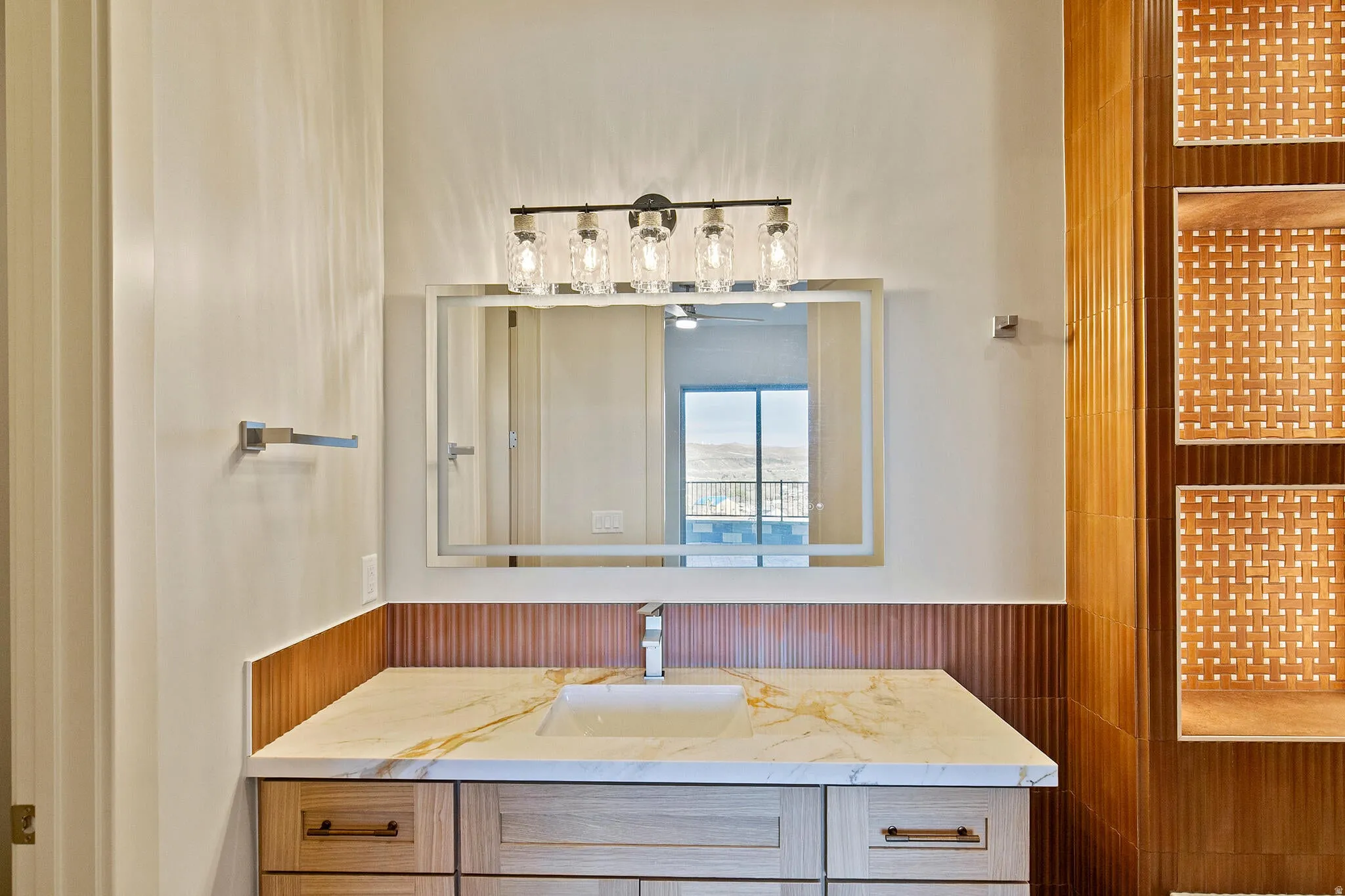 Bathroom vanity featuring a light-toned wood-finish cabinet with drawer storage, a white countertop with gold veining, and an undermount sink with a chrome faucet