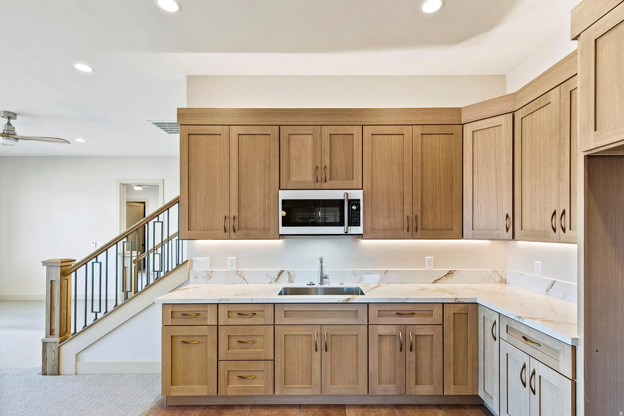 Kitchenette featuring a stainless steel sink, under-cabinet lighting, and light wood-tone cabinetry