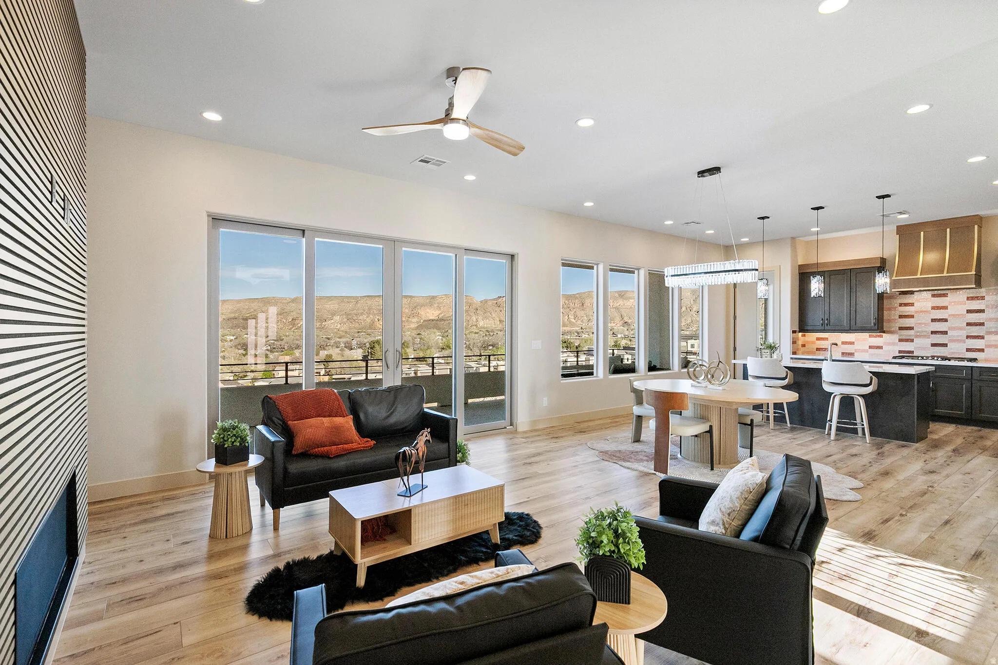 Open-concept living space featuring wood-finish flooring, a linear fireplace with a textured accent wall, and a ceiling fan