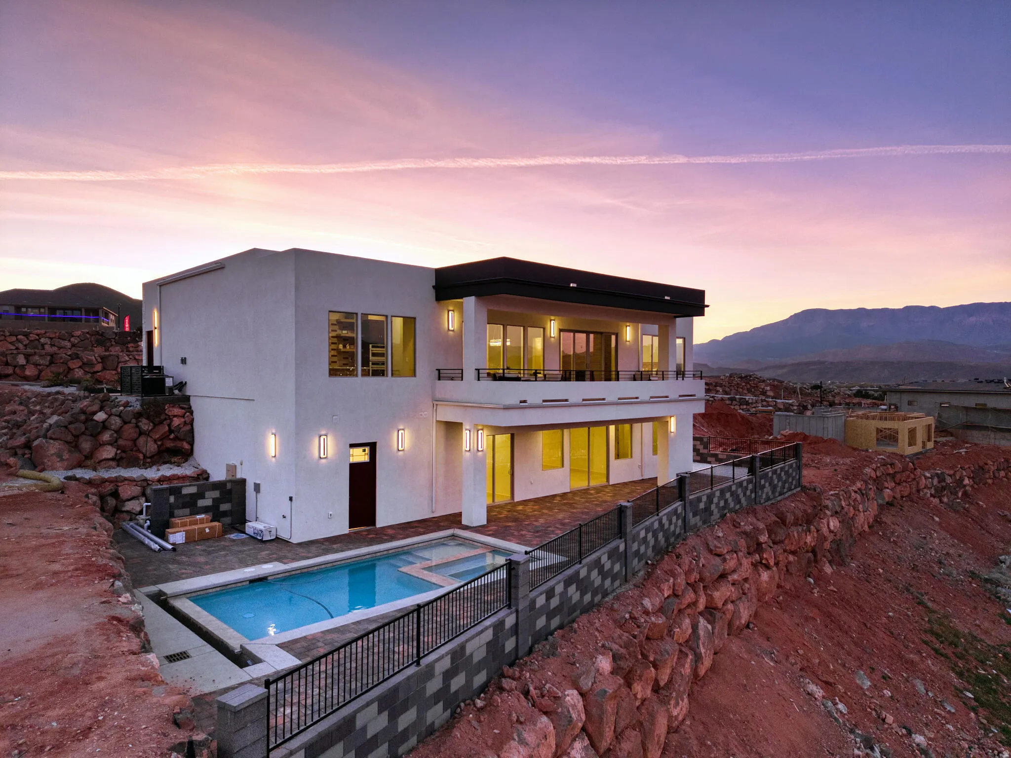 Contemporary multi-level residence featuring a rectangular swimming pool, an upper-level balcony, a lower-level patio, and exterior wall sconces