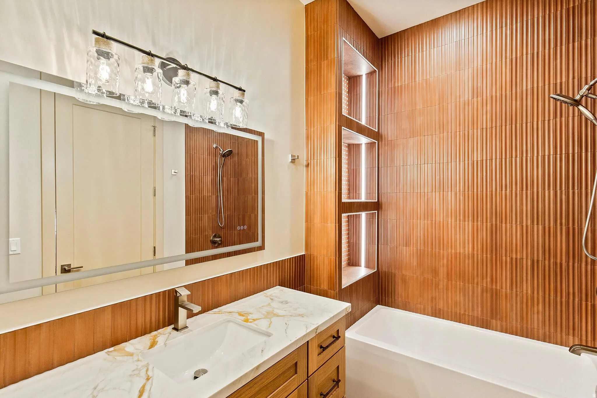Bathroom featuring a white rectangular undermount sink, a marble-patterned countertop, light wood cabinetry with dark hardware, and a chrome faucet