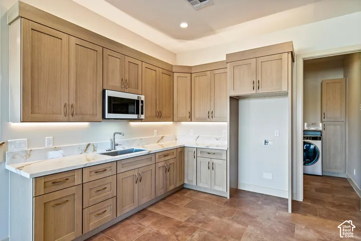 Kitchenette featuring light wood-finish cabinetry, under-cabinet lighting, a stainless-steel microwave, and light-toned countertops with an integrated sink