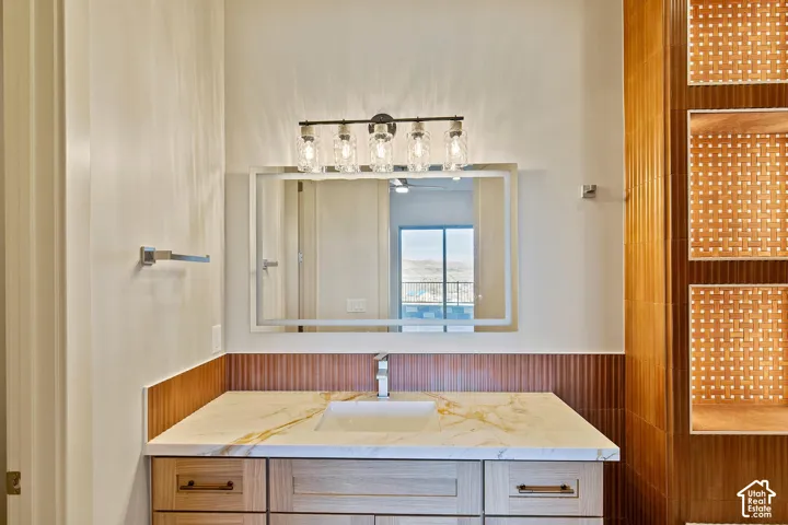 Bathroom vanity featuring a light-toned wood-finish cabinet with drawer storage, a white countertop with gold veining, and an undermount sink with a chrome faucet