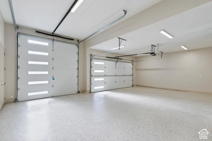 Spacious garage featuring two overhead doors with integrated light panels, an epoxy-coated concrete floor, and multiple ceiling-mounted fluorescent light fixtures