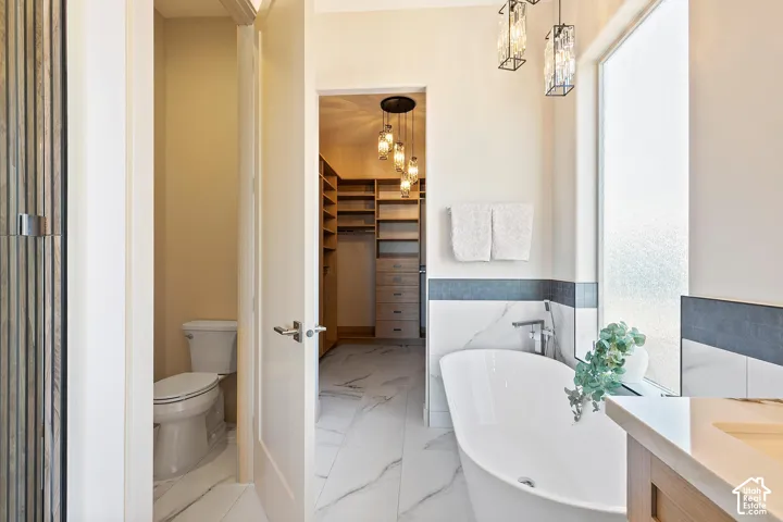 Freestanding soaking tub with chrome fixtures, framed by marble-look wall tiling and a frosted privacy window