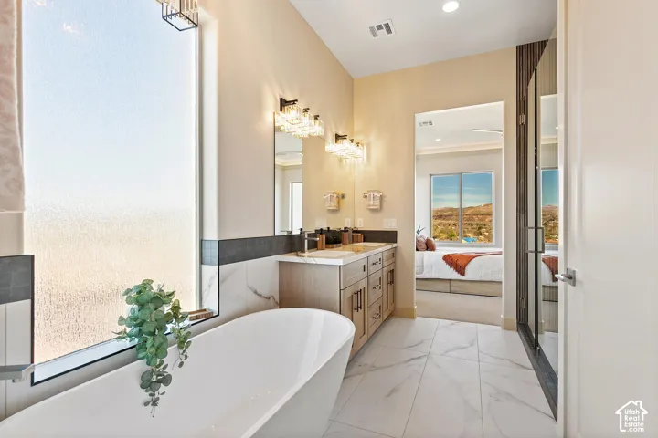 Freestanding bathtub with an expansive frosted window, dual vanity with undermount sinks, decorative light fixtures, and marble-finish tile flooring