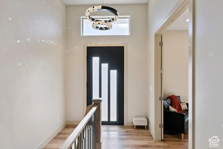 Entryway featuring a modern black door with vertical glass inserts, transom window, contemporary chandelier, wood-finish flooring, and a staircase with a wooden handrail and metal balusters