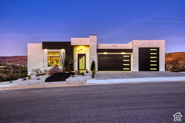 Modern architectural home featuring a multi-tone exterior, two integrated garage doors with horizontal light accents, and xeriscaped landscaping