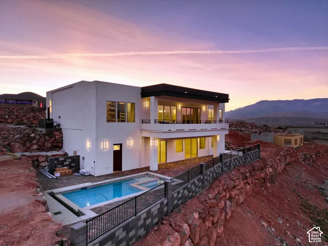 Contemporary multi-level residence featuring a rectangular swimming pool, an upper-level balcony, a lower-level patio, and exterior wall sconces