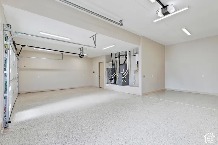 Spacious garage featuring a durable epoxy floor coating, multiple overhead lighting fixtures, exposed garage door mechanisms, and a utility area with visible mechanical systems