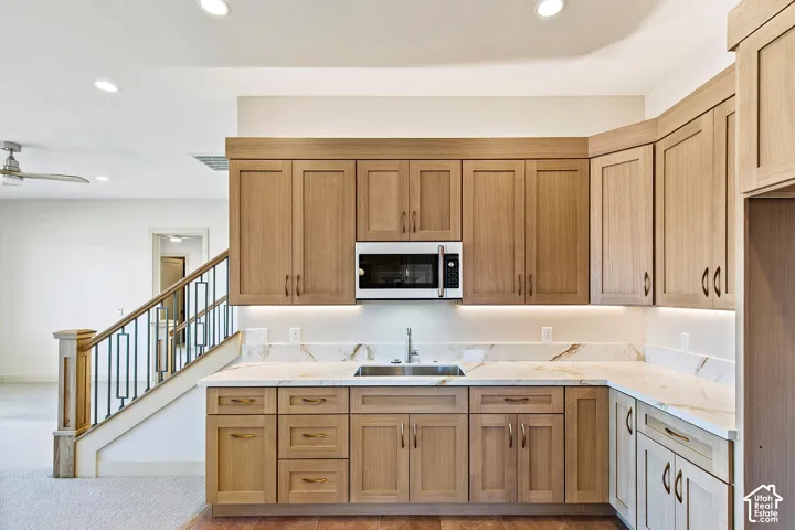 Kitchenette featuring a stainless steel sink, under-cabinet lighting, and light wood-tone cabinetry