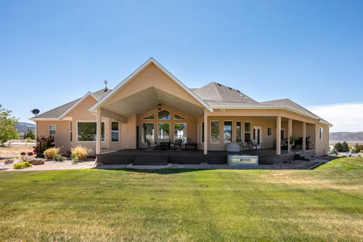 Expansive rear exterior featuring a covered patio, a full-width deck, and a large grassy area