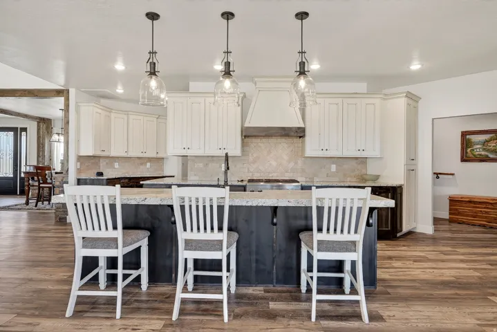 Kitchen featuring a large island with seating, pendant lighting, white upper cabinetry, and a herringbone tile backsplash