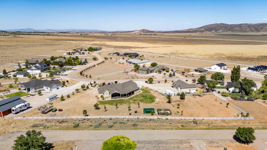 Expansive rural landscape featuring scattered residential properties, paved and unpaved roads, and distant mountains under a clear sky