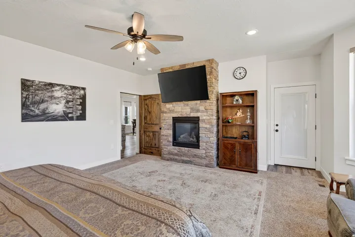 Stone-clad fireplace with mounted television, ceiling fan, recessed lighting, and wood-finish flooring