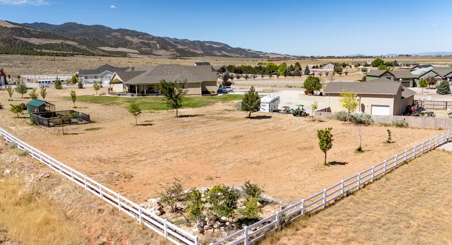 Expansive property featuring a ranch-style residence with a covered patio, a separate outbuilding, a white picket fence, a small fenced enclosure, and surrounding open terrain with distant mountains