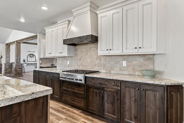 Gourmet kitchen featuring a built-in stainless steel gas range, herringbone tile backsplash, granite countertops, and two-tone cabinetry with upper white and lower dark wood-finish