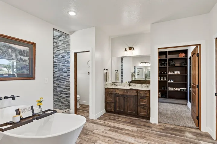 Bathroom featuring a freestanding tub, a walk-in shower with tile surround, a double vanity with stone countertop, wood-finish flooring, and a walk-in closet with built-in shelving