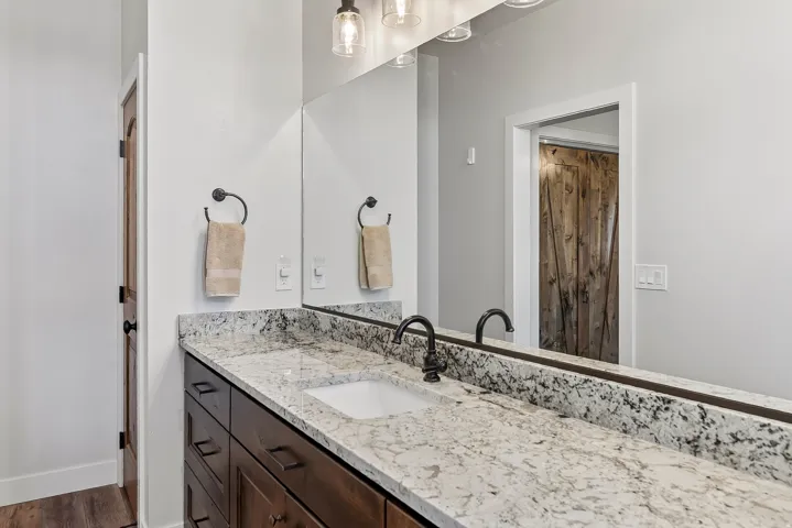 Bathroom vanity featuring a light-toned stone countertop, integrated rectangular sink, dark bronze faucet, and a large wall-mounted mirror