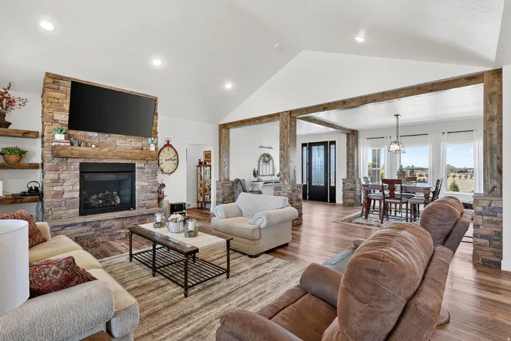 Spacious living area featuring a stone-clad fireplace with a wood mantle, wood-finish flooring, vaulted ceilings, and recessed lighting