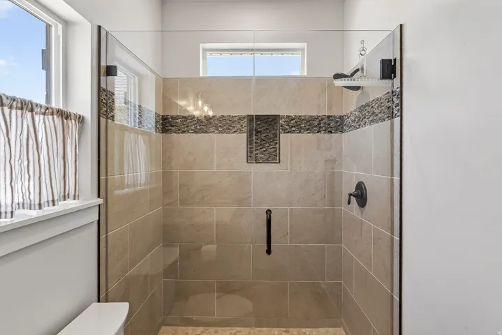 Glass-enclosed shower featuring large format wall tiles, a mosaic accent band, a built-in niche, and a rain shower head with matte black fixtures