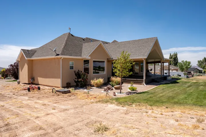 Rear exterior featuring a covered patio, stucco siding, a composition shingle roof, large windows, and a landscaped patio area