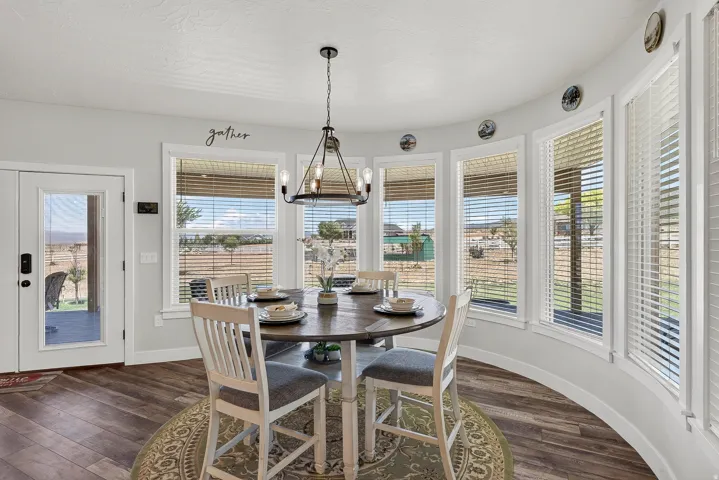 Dining area featuring a curved wall of multiple windows with horizontal blinds, a glass-paned door, wood-finish flooring, and a modern chandelier