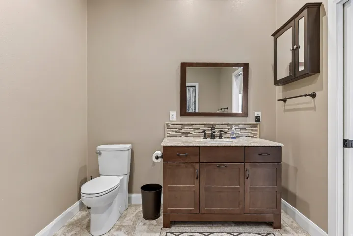 Powder room featuring a dark wood vanity with a light-toned countertop, a rectangular framed mirror, and a mosaic tile backsplash