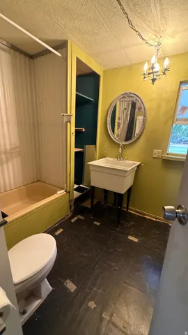 Drop-in bathtub, pedestal sink, wall-mounted mirror, and overhead chandelier fixture