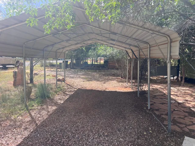 Metal-framed carport with a corrugated roof, featuring a gravel driveway and flagstone pathway