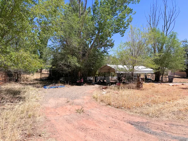 Outdoor property featuring a gravel driveway, mature trees, a metal carport structure, and perimeter fencing