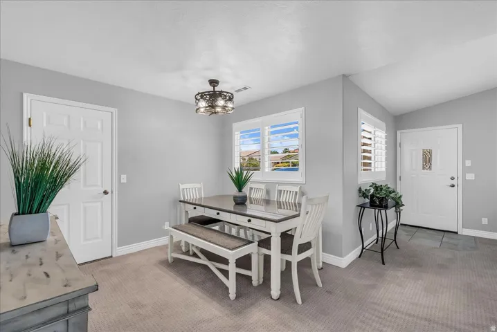 Carpeted dining area featuring a decorative chandelier, white plantation shutters, and a tiled entryway