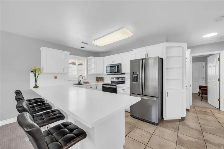 Kitchen featuring a large breakfast bar, white cabinetry, stainless steel appliances, and tile flooring