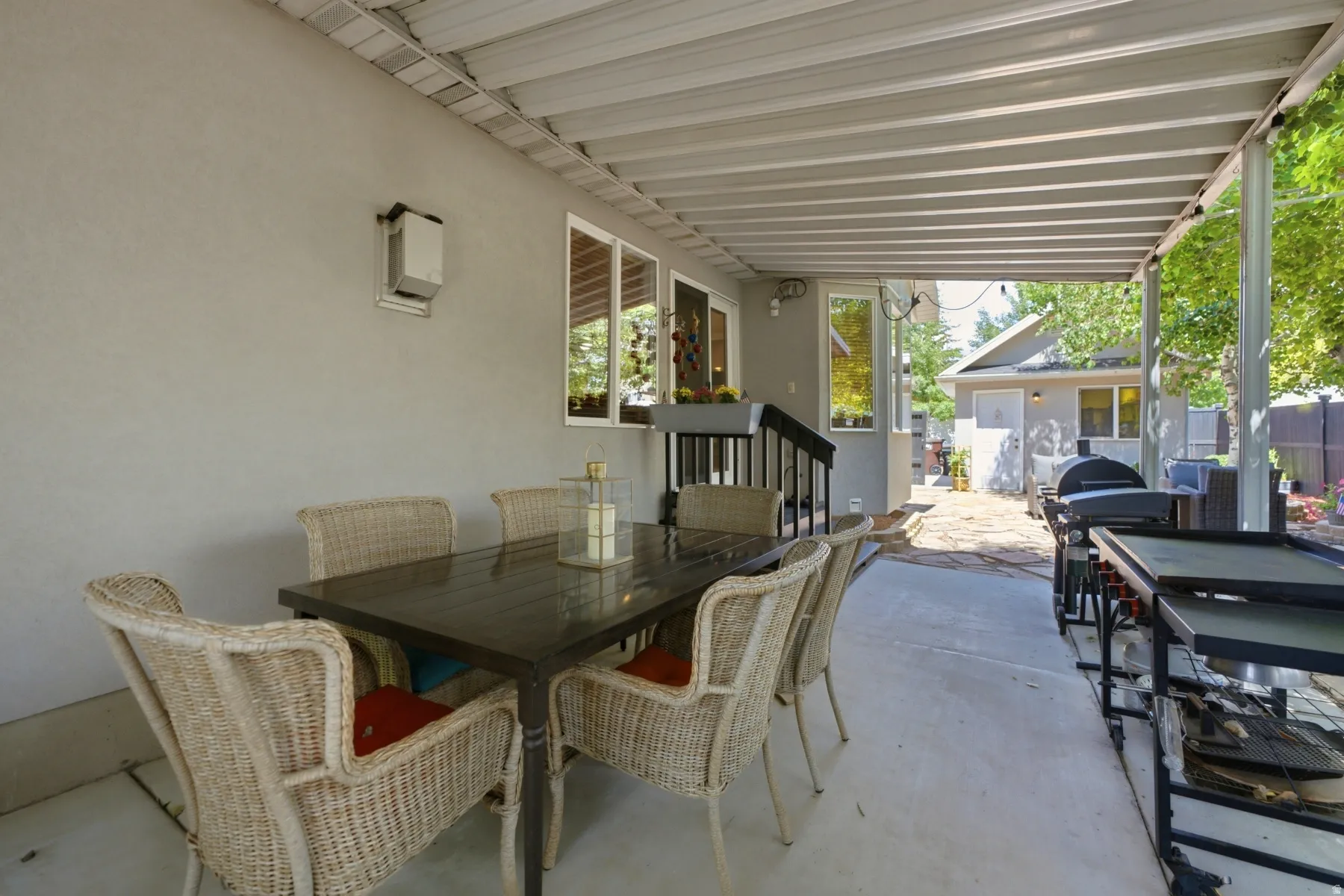 Covered concrete patio featuring a textured stucco exterior, multiple large windows, and an outdoor wall-mounted light fixture