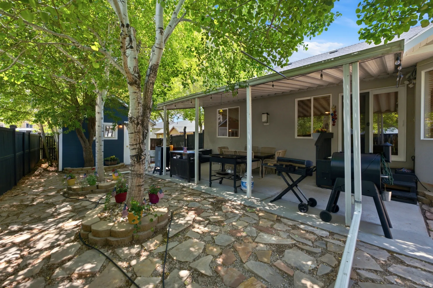 Covered patio with a concrete slab, stone paver ground covering, mature trees, and a privacy fence