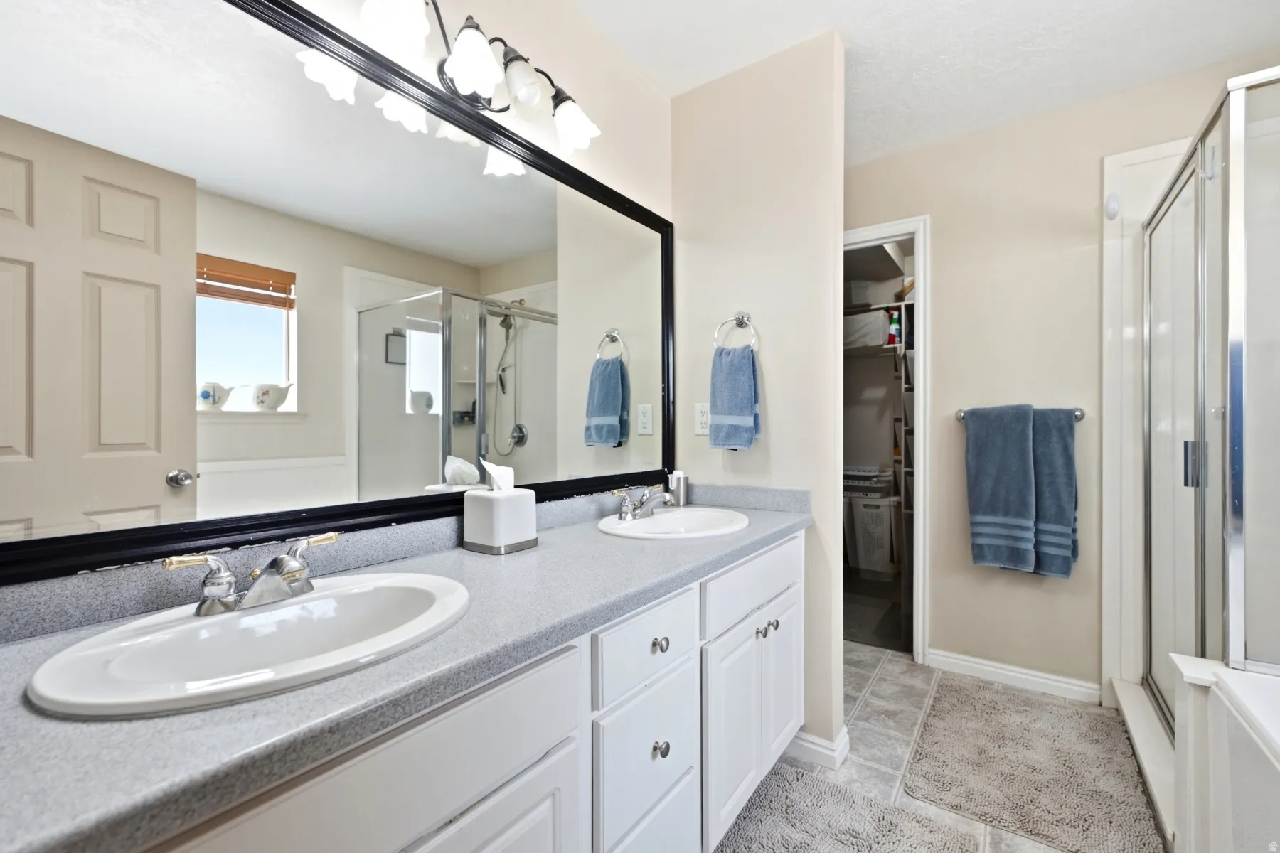 Primary Suite with double vanity with light gray countertop, white cabinetry, and a large framed mirror