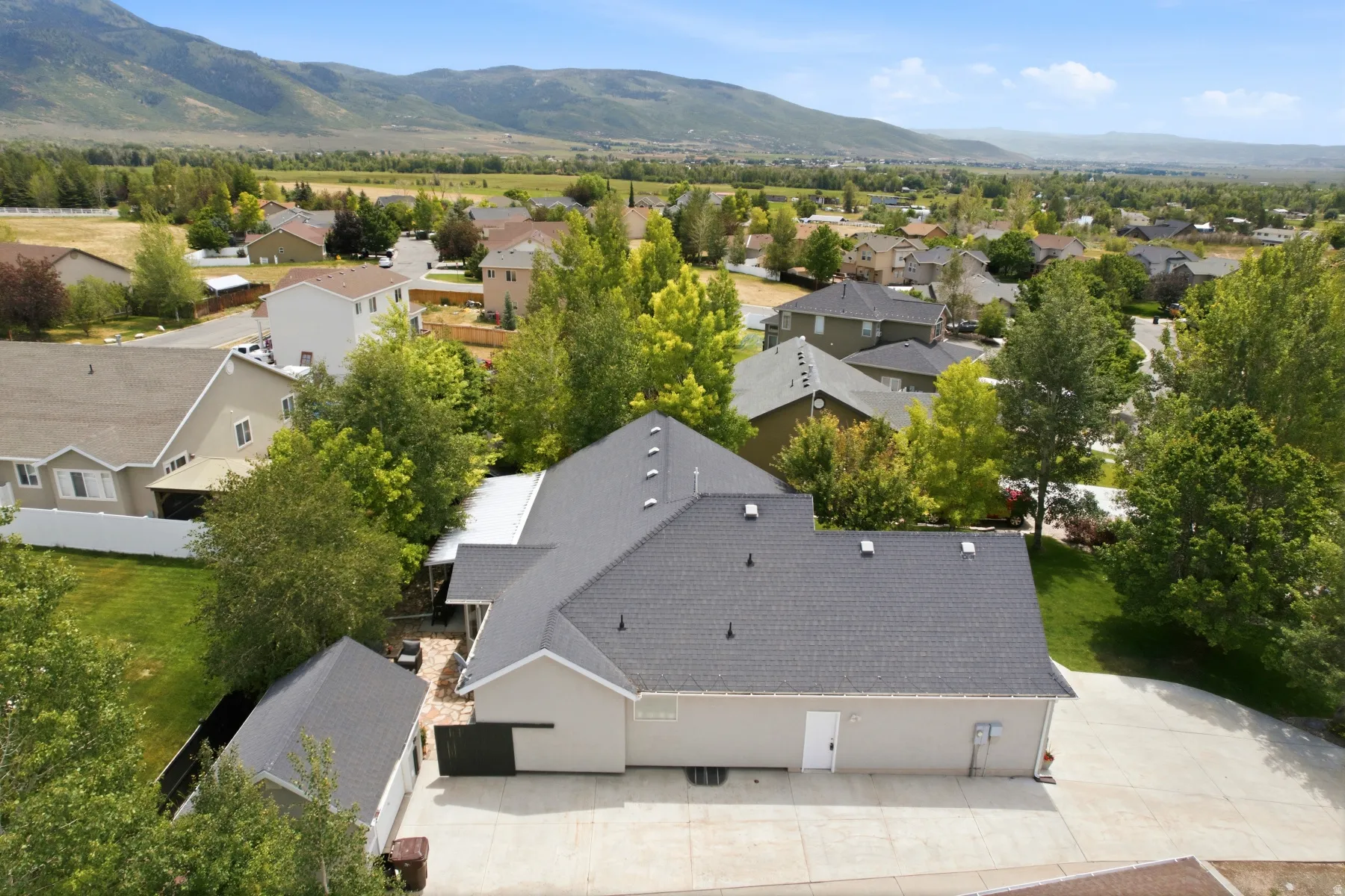 Aerial property perspective featuring a neutral-toned exterior, dark shingled roofs, and an expansive concrete driveway