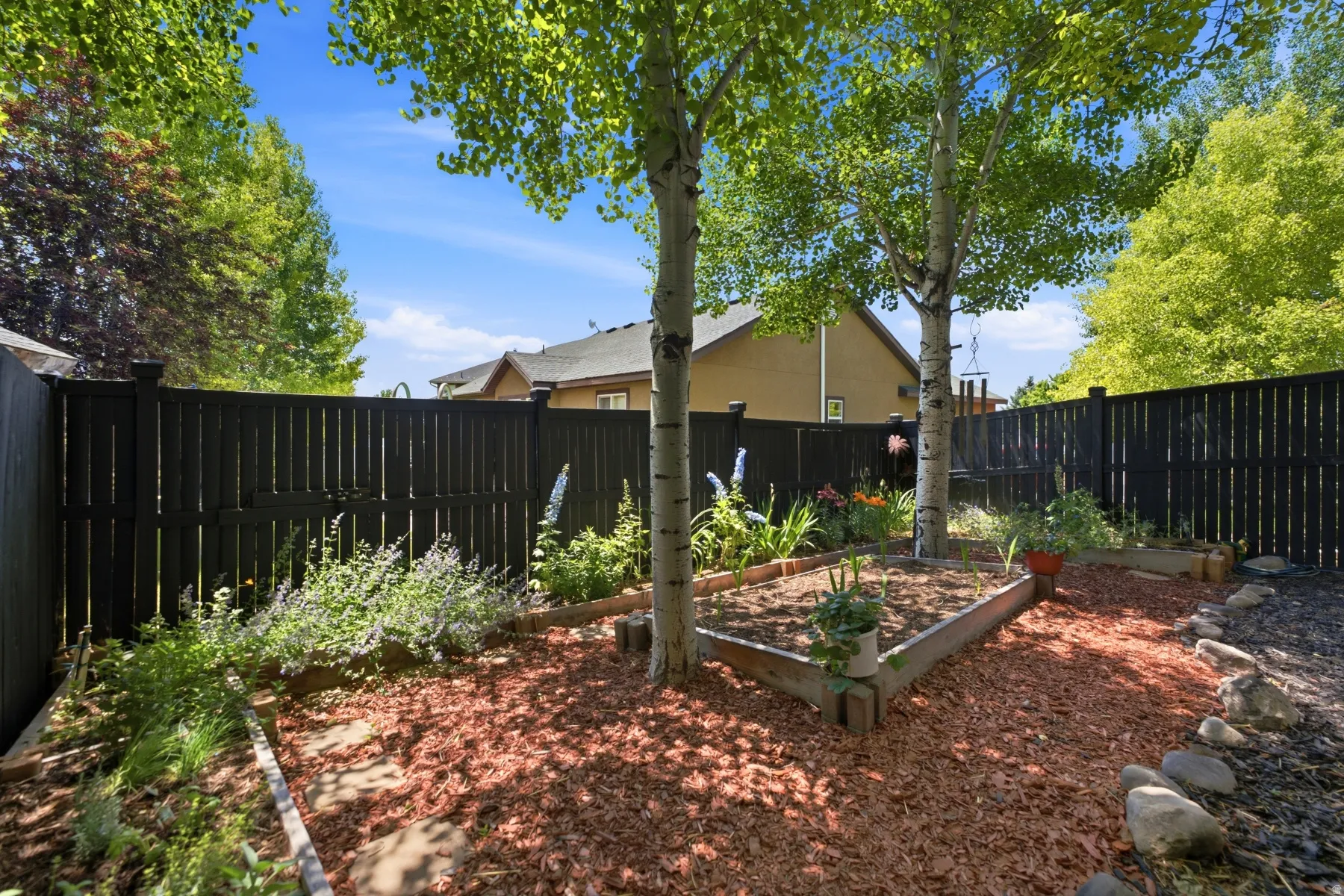 Fenced yard featuring a wooden privacy fence, mature trees, wood-edged garden beds, and ground cover