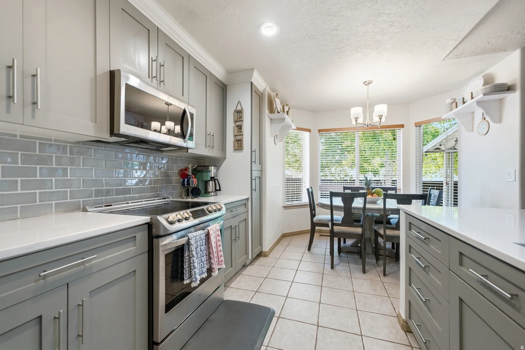 Contemporary kitchen featuring gray shaker cabinetry, stainless steel appliances, a subway tile backsplash, and light-tone countertops