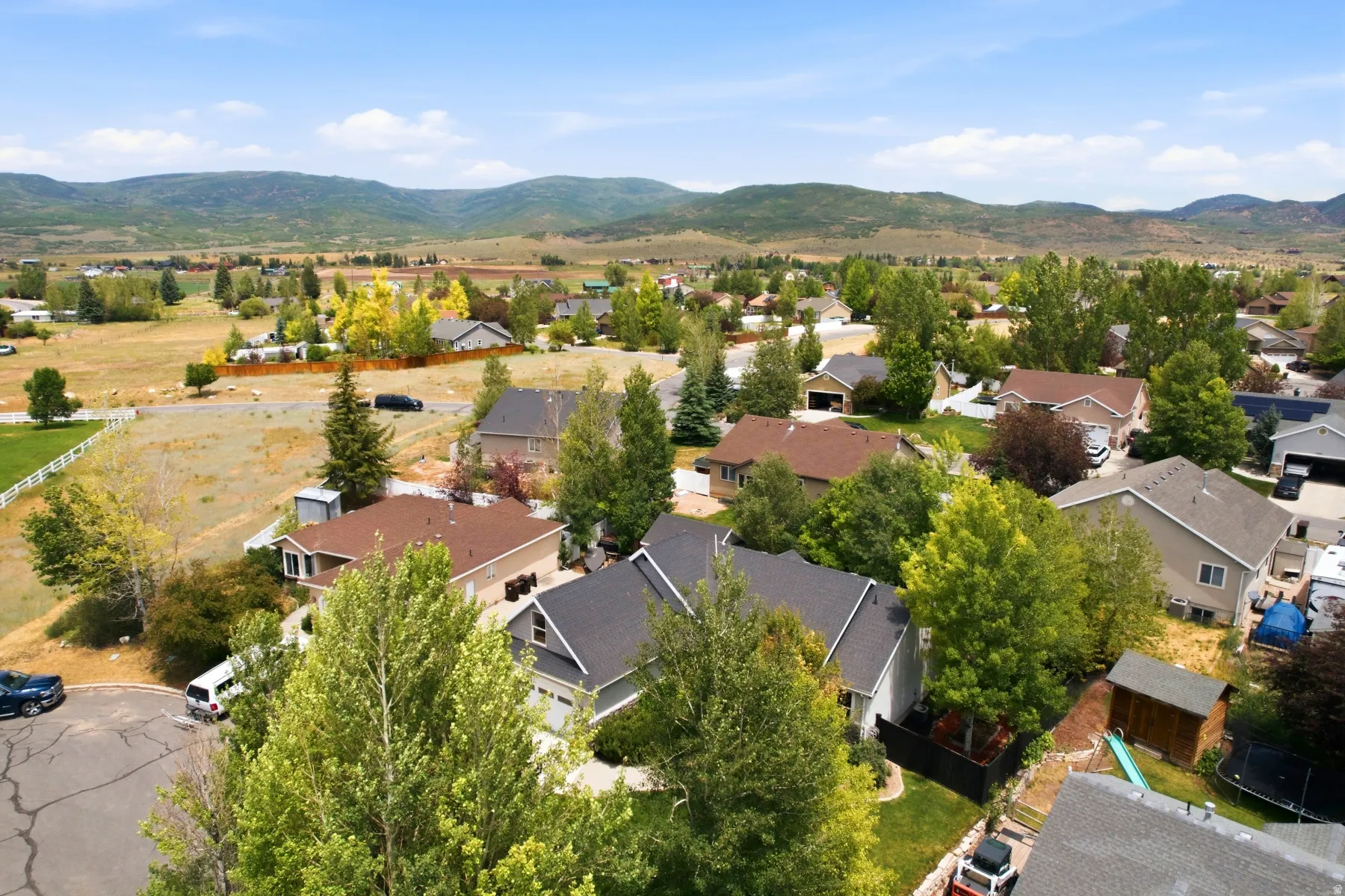 Suburban neighborhood featuring residences with varied architectural styles and mature landscaping, framed by distant mountains and open fields