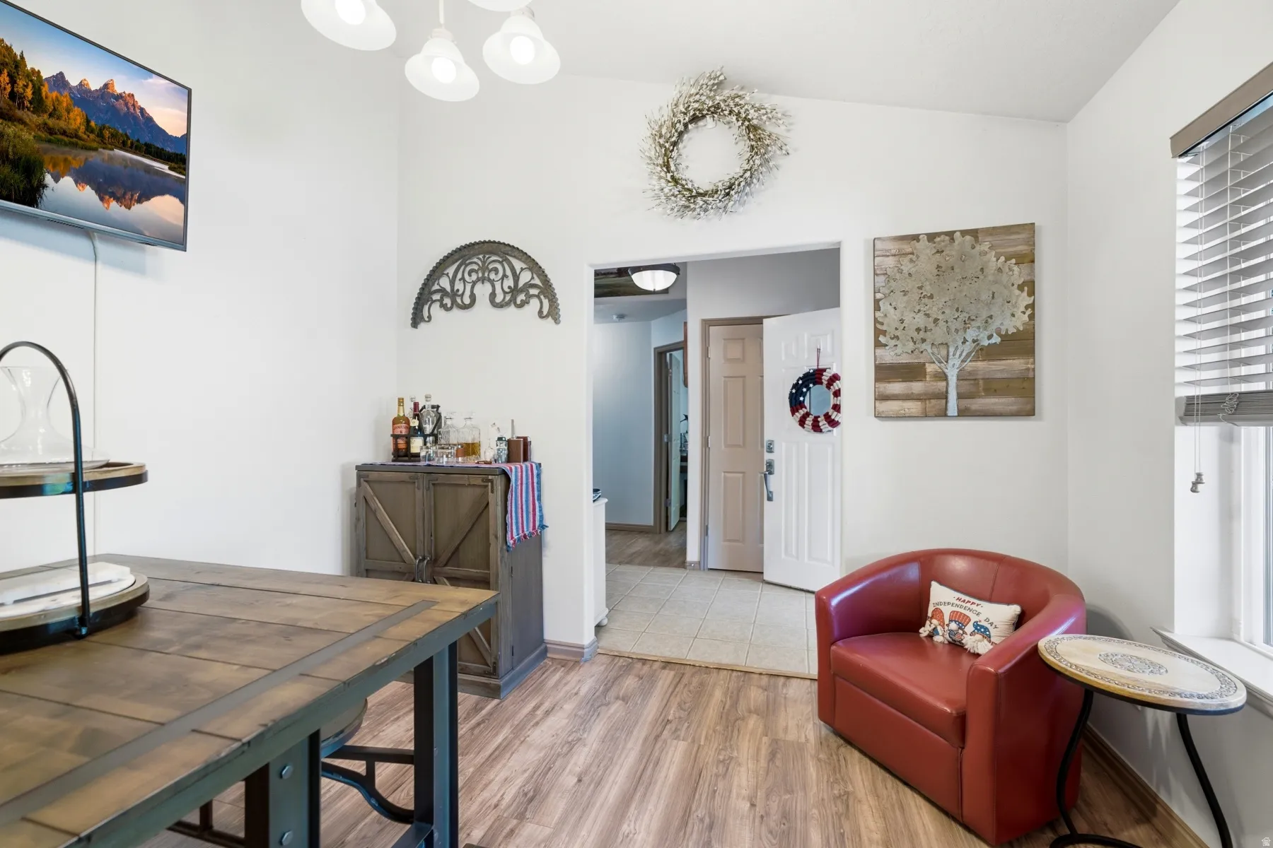 Vaulted ceiling with a four-light fixture, wood-finish flooring, white painted walls, and a window with horizontal blinds